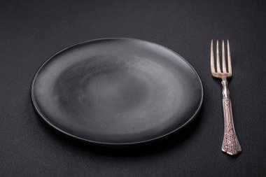 Empty ceramic round plate on dark textured concrete background. Cutlery, preparation for dinner
