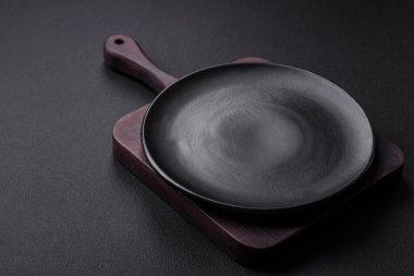 Empty ceramic round plate on dark textured concrete background. Cutlery, preparation for dinner