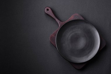 Empty ceramic round plate on dark textured concrete background. Cutlery, preparation for dinner