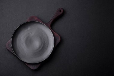 Empty ceramic round plate on dark textured concrete background. Cutlery, preparation for dinner