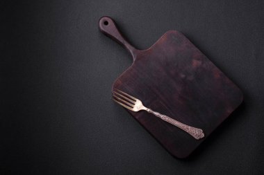 Empty wooden cutting board on dark textured concrete background. Cutlery, preparation for dinner