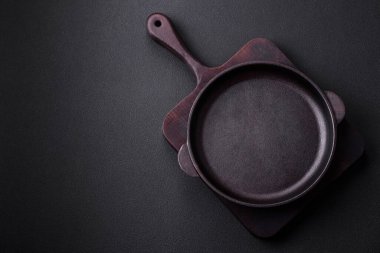 Empty round cast iron skillet on dark textured concrete background. Cutlery, preparation for dinner