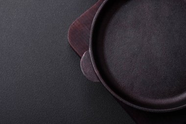 Empty round cast iron skillet on dark textured concrete background. Cutlery, preparation for dinner