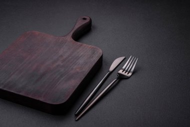 Empty wooden cutting board on dark textured concrete background. Cutlery, preparation for dinner