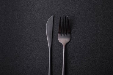 Metal kitchen knife and fork on a dark textured concrete background. Cutlery, preparation for dinner