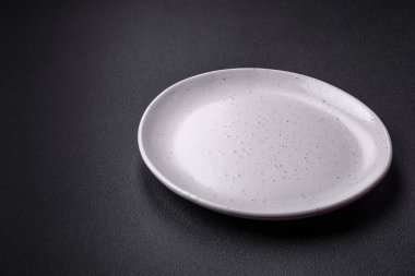 Empty ceramic round plate on dark textured concrete background. Cutlery, preparation for dinner