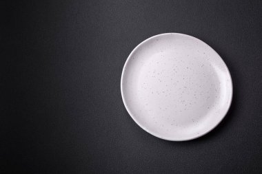 Empty ceramic round plate on dark textured concrete background. Cutlery, preparation for dinner