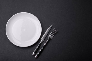 Empty ceramic round plate on dark textured concrete background. Cutlery, preparation for dinner