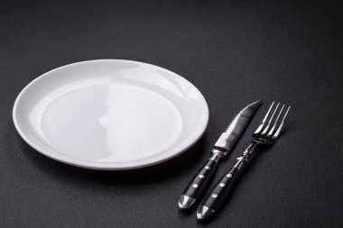 Empty ceramic round plate on dark textured concrete background. Cutlery, preparation for dinner