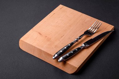 Empty wooden cutting board on dark textured concrete background. Cutlery, preparation for dinner