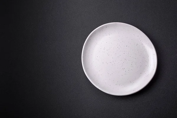 Empty ceramic round plate on dark textured concrete background. Cutlery, preparation for dinner