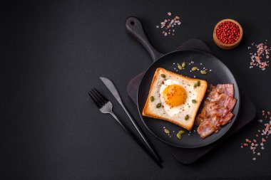Kalp şeklinde kızarmış yumurta ve susamlı tost, keten tohumu ve balkabağı çekirdeği siyah bir tabakta koyu beton arka planda.