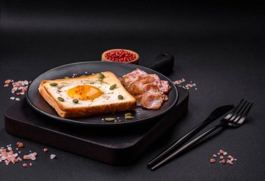 Kalp şeklinde kızarmış yumurta ve susamlı tost, keten tohumu ve balkabağı çekirdeği siyah bir tabakta koyu beton arka planda.