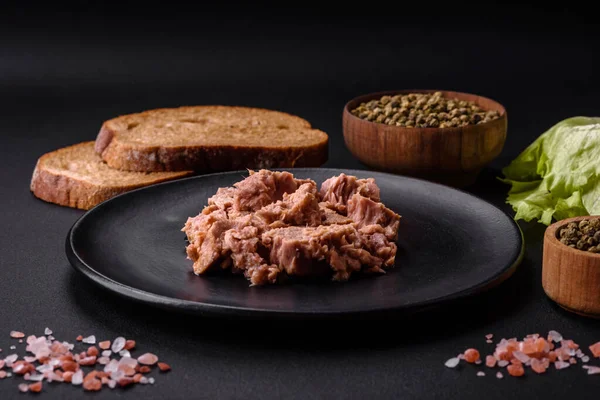 Delicious canned tuna meat on a black ceramic plate on a dark concrete background. Healthy food preparation