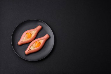 Composite concept of fried eggs inside a cut sausage with spices on a black ceramic plate on a dark concrete background