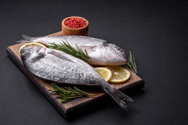 Fresh raw dorado fish with spices, herbs, salt and lemon on a dark concrete background