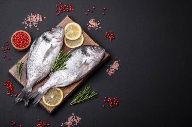 Fresh raw dorado fish with spices, herbs, salt and lemon on a dark concrete background