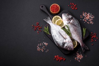 Fresh raw dorado fish with spices, herbs, salt and lemon on a dark concrete background