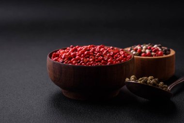 Composition, concept, consisting of several types of different colors of allspice in bowls and spoons on a dark concrete background