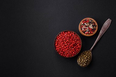 Composition, concept, consisting of several types of different colors of allspice in bowls and spoons on a dark concrete background