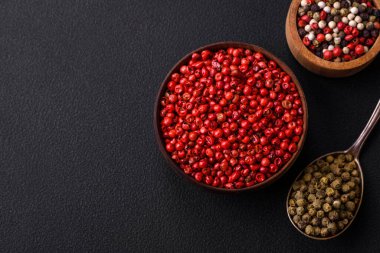 Composition, concept, consisting of several types of different colors of allspice in bowls and spoons on a dark concrete background