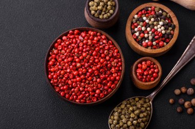 Composition, concept, consisting of several types of different colors of allspice in bowls and spoons on a dark concrete background