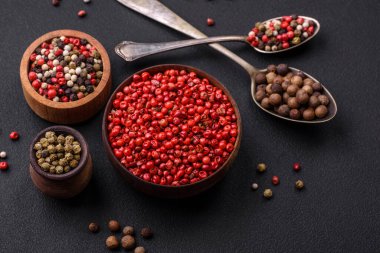 Composition, concept, consisting of several types of different colors of allspice in bowls and spoons on a dark concrete background