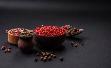 Composition, concept, consisting of several types of different colors of allspice in bowls and spoons on a dark concrete background