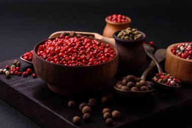Composition, concept, consisting of several types of different colors of allspice in bowls and spoons on a dark concrete background