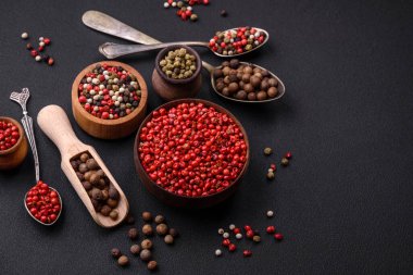 Composition, concept, consisting of several types of different colors of allspice in bowls and spoons on a dark concrete background