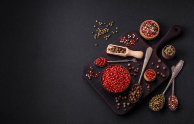 Composition, concept, consisting of several types of different colors of allspice in bowls and spoons on a dark concrete background