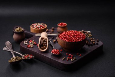 Composition, concept, consisting of several types of different colors of allspice in bowls and spoons on a dark concrete background