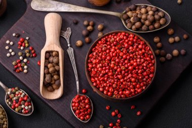 Composition, concept, consisting of several types of different colors of allspice in bowls and spoons on a dark concrete background