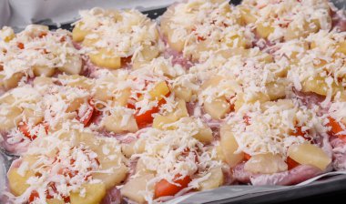 A dish consisting of meat, tomatoes, pineapple, cheese, spices and herbs on parchment on a baking sheet. Preparing food for baking in the oven