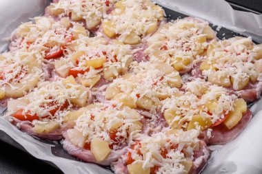 A dish consisting of meat, tomatoes, pineapple, cheese, spices and herbs on parchment on a baking sheet. Preparing food for baking in the oven