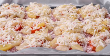 A dish consisting of meat, tomatoes, pineapple, cheese, spices and herbs on parchment on a baking sheet. Preparing food for baking in the oven