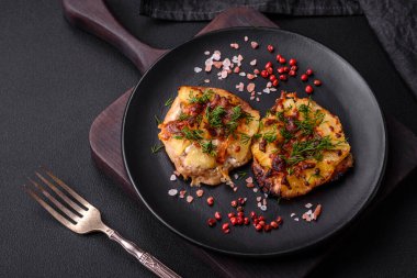 Meat baked in the oven with pineapple, tomatoes, cheese, spices and herbs on a black ceramic plate on a dark concrete background