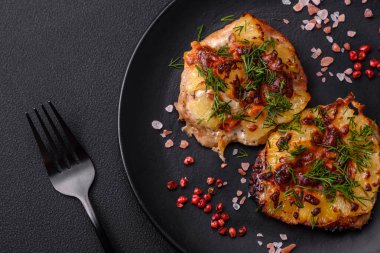 Meat baked in the oven with pineapple, tomatoes, cheese, spices and herbs on a black ceramic plate on a dark concrete background