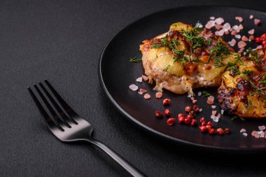 Meat baked in the oven with pineapple, tomatoes, cheese, spices and herbs on a black ceramic plate on a dark concrete background