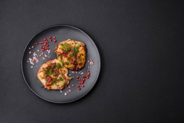 Meat baked in the oven with pineapple, tomatoes, cheese, spices and herbs on a black ceramic plate on a dark concrete background