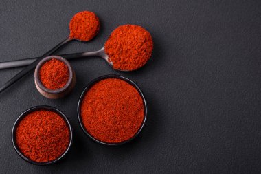 Spice smoked paprika in the form of powder in bowls and spoons on a dark concrete background. Asian cuisine ingredients