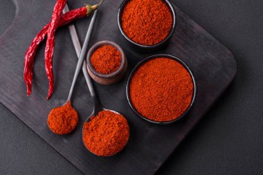 Spice smoked paprika in the form of powder in bowls and spoons on a dark concrete background. Asian cuisine ingredients