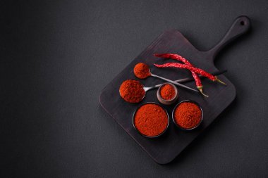 Spice smoked paprika in the form of powder in bowls and spoons on a dark concrete background. Asian cuisine ingredients