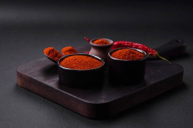 Spice smoked paprika in the form of powder in bowls and spoons on a dark concrete background. Asian cuisine ingredients
