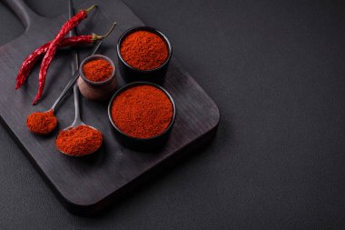 Spice smoked paprika in the form of powder in bowls and spoons on a dark concrete background. Asian cuisine ingredients