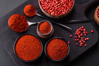 Spice smoked paprika in the form of powder in bowls and spoons on a dark concrete background. Asian cuisine ingredients
