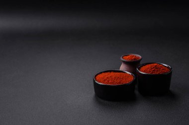 Spice smoked paprika in the form of powder in bowls and spoons on a dark concrete background. Asian cuisine ingredients