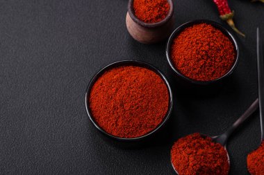 Spice smoked paprika in the form of powder in bowls and spoons on a dark concrete background. Asian cuisine ingredients