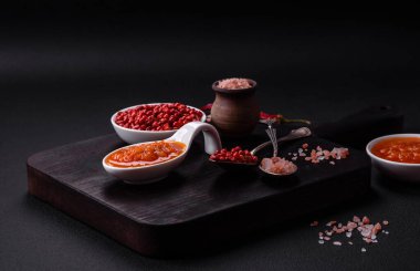 Red adjika sauce or ketchup with spices and herbs on a dark concrete background