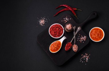 Red adjika sauce or ketchup with spices and herbs on a dark concrete background